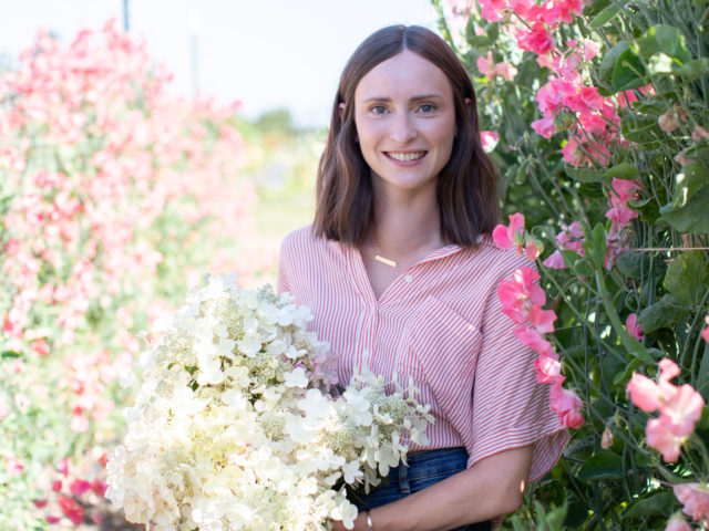 Laura Davis holding white hydrangeas in a row of sweet peas at Floret